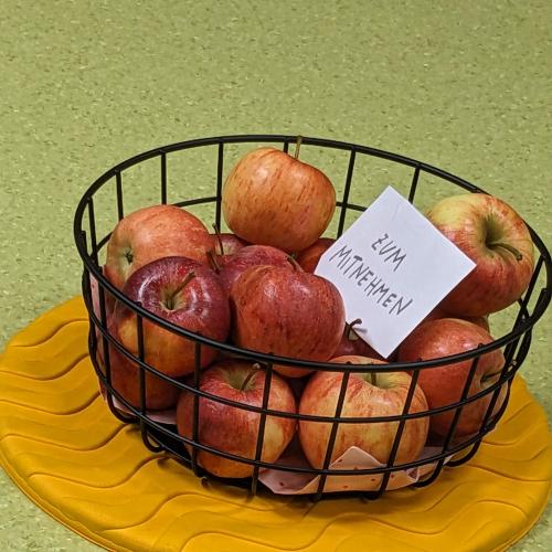 Man sieht einen Korb mit Äpfeln. Dabei liegt ein Zettel it dem Text:: Zum Mitnehmen