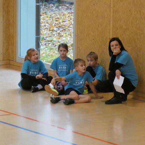 4 SchülerInnen sitzen im Turnsaal mit ihrer Lehrerin als Zuschauer am Boden 