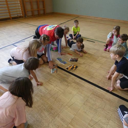Turnsaal - Die Kinder mit dem Betreuer sind über "Schlangenbildern" gebeugt