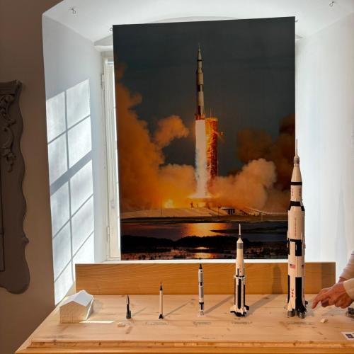 Vor dem Bild einer startenden Rakete stehen verschiedene Modelle von Raketen
