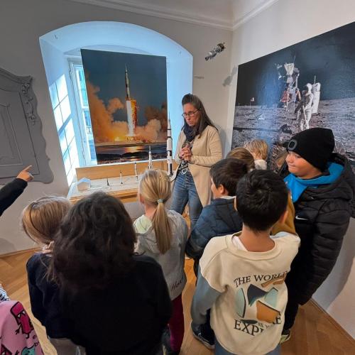 Einige Kinder stehen mit der Museumspädagogin vor den Bildern einer startenden Rakete und von der Mondoberfläche