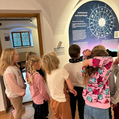 Kinder stehen vor einem Bild über Astologie - Sternkreiszeichen