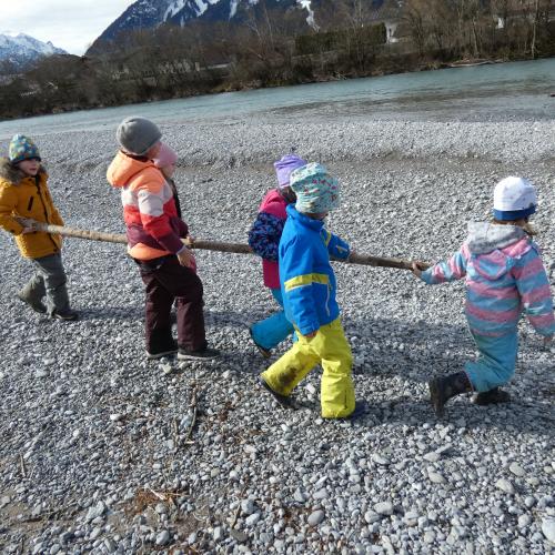 Sechs kinder gehen mit einem Baumstamm zum Lech, um ihn hineinzuwerfen