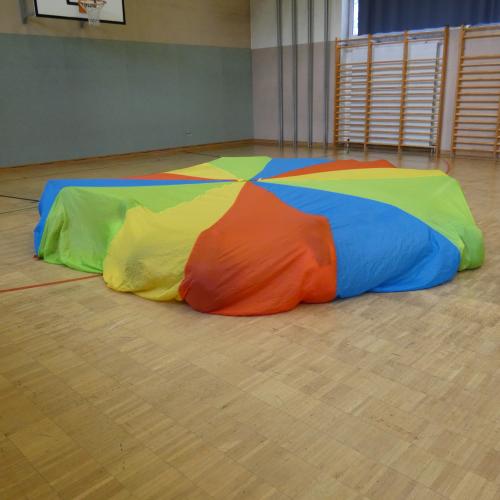 Man sieht im TUrnsaal nur das bunte Fallschirmtuch unter dem die Kinder versteckt sind
