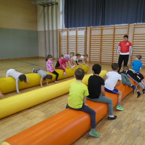 Kinder sitzen oder liegen auf dicken aufgeblasenen Luftwürsten im Turnsaal