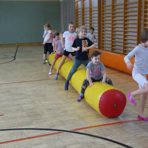 Kinder hüpfen im Turnsaal auf einer dicken gelben aufblasbaren Luftwurst