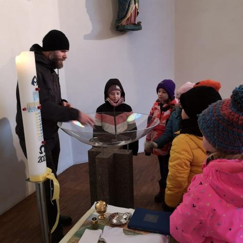 Der Diakon mit einigen Kindern vor dem Taufbecken