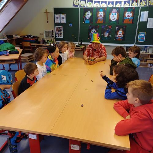 Verkleidete Kinder sitzen mit Lehrer an einem Tisch bei einem Spiel
