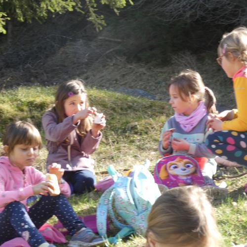 EInige Kinder auf einer Wiese sitzend - sie essen ihre Jause