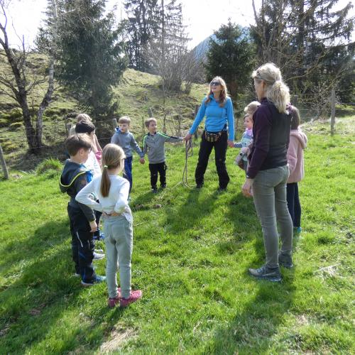 Kinder stehen mit Naturpädagoginnen auf einer Frühlingswiese und besprechen ein Spiel