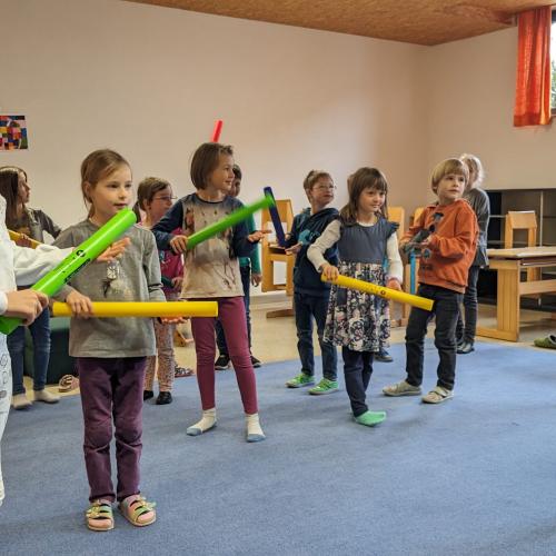 Kinder stehen im Bewegungsraum im Kreis und machen Musik mit den Boomwhackers