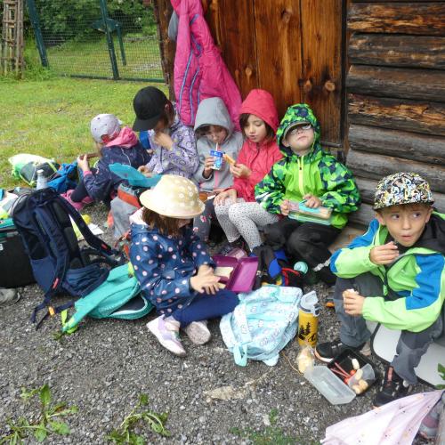 Kinder sitzen an einer Stadelwand und jausnen