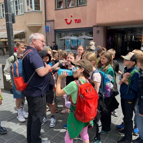Kinder stehen in der Maria Theresienstraße um den Lehrer, der etwas erklärt