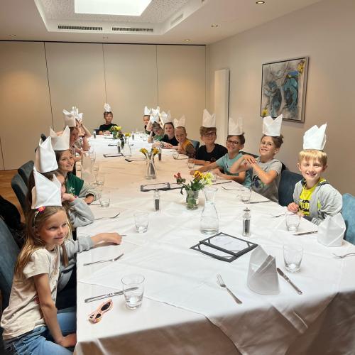 Essen im Gasthof Sailer. die Kinder haben die gefalteten Servietten wie Bischofsmützen am Kopf