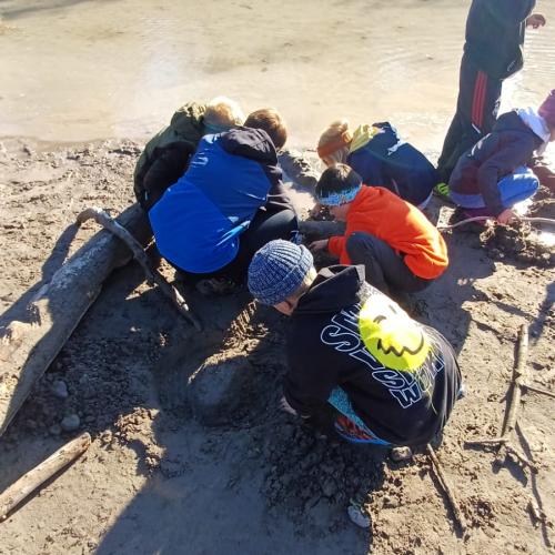 6 Kinder hocken am Boden im Sand und bauen einen Wildfluss nach