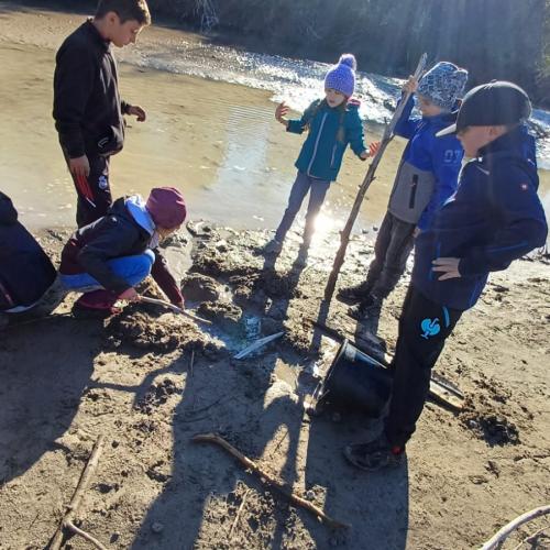5 KInder stehen im Sand am Lech, im Hintergrund Wasser und Sonnenstrahlen