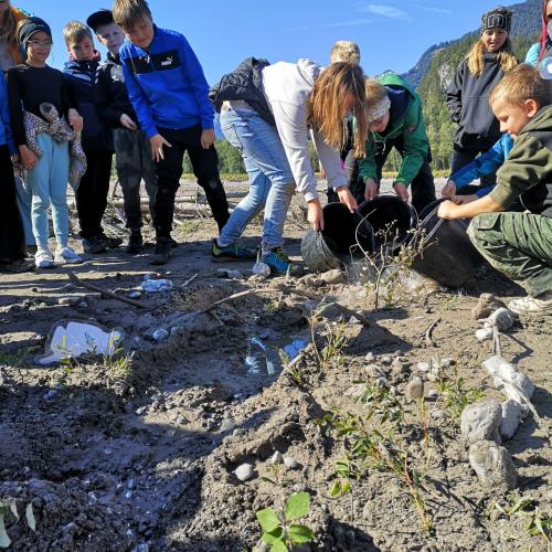 Eine Gruppe von Kindern baut mit Sand und Steinen einen Wildfluss nach