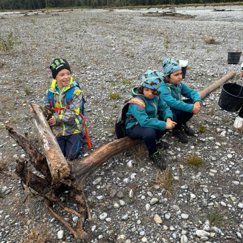 3 Buben sitzen auf einem Baumstamm auf einer Schotterbank am Lech