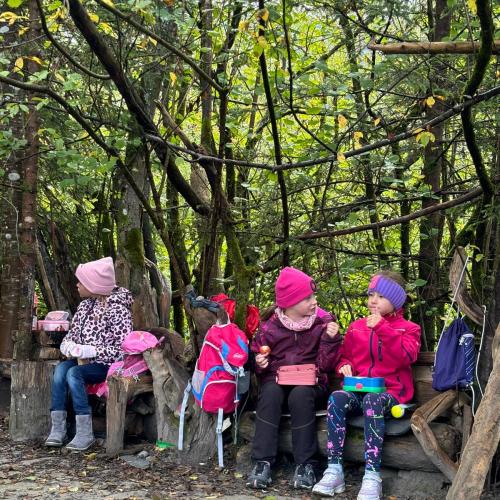 Einige Kinder sitzen auf Holzstämmen im Auwald und essen ihre Jause