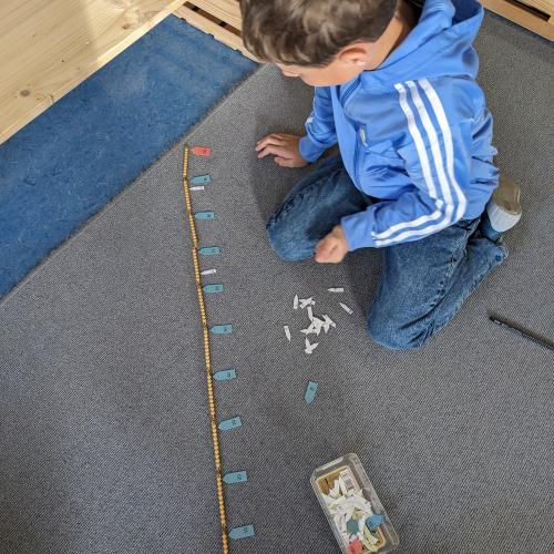 Ein Bub sitzt am Teppich und legt zur Montessori 100erKette Ziffernkärtchen