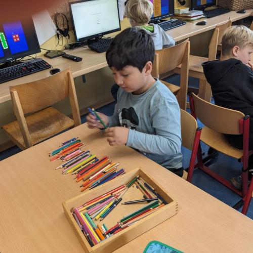 Ein Bub sitzt beim Tisch und sortiert Buntstifte und bündelt sie