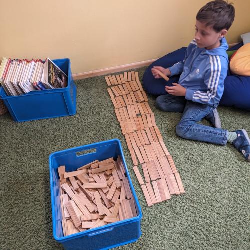 EIn Bub sitzt am grünen Teppich und hat 100 Kapplabausteine in Reihen aufgelegt