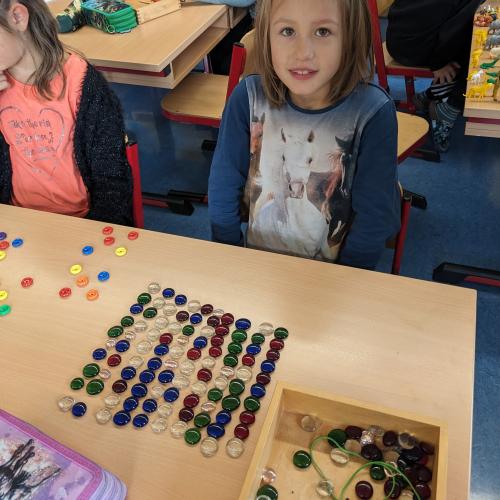 Ein Kind sitzt beim Tisch und hat 100 Glasmuggelsteine in Reihen aufgelegt