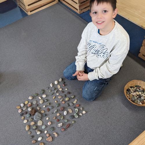 Ein Junge hat am Teppich 100 Steine in Reihen ordentlich aufgelegt