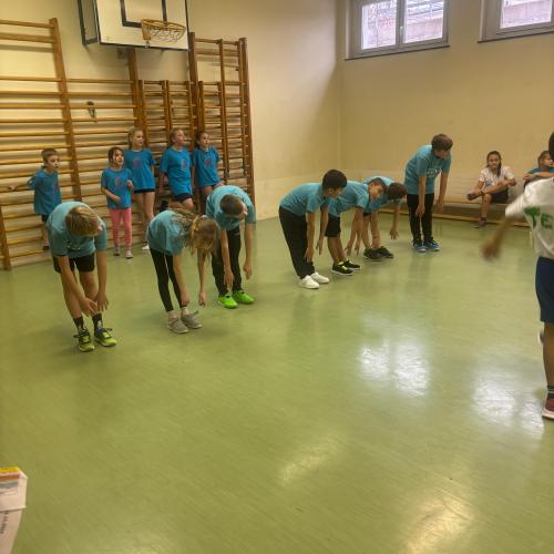 Einige SchülerInnen beim Aufräumen in einem Gymnastikraum mit grünem Boden, im Hintergrund stehen einige SchülerInnen an der Sprossenwand