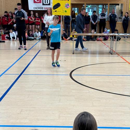 Ein Schüler in kurzer turnhose und blauem Schul T-Shirt geht mit dem Klassenschild zur Siegerehrung