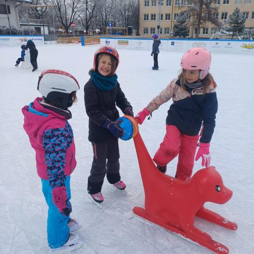 3 Mädchen stehen am Eisplatz rund um einen roten Schiebehund