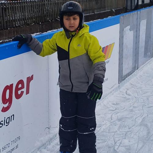 Ein Jiunge, das erste Mal am Eis, hält sich an der Bande fest