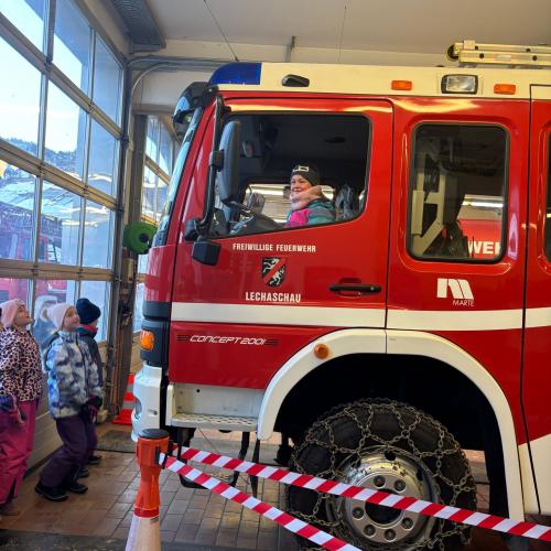 Ein Kind sitzt im Feuerwehrauto in der Garage, andere Kinder stehen vor dem Auto