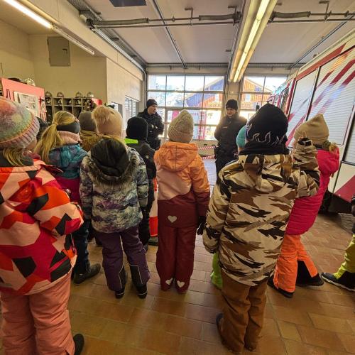 Die Schulkinder stehen in der Garage der Feuerwehr und hören den Erklärungen von 2 Polizisten zu