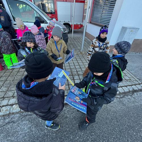 Kinder stehen mit Unterlagen zur Kinderpolizei am Parkplatz der Feuerwehr Lechaschau dahinter ein Polizei- und ein Feuerwehrauto