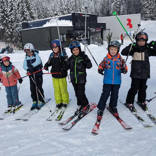7 Kinder stehen als Gruppe zusammen vor dem Lift - Stöcke hochgeb´hoben