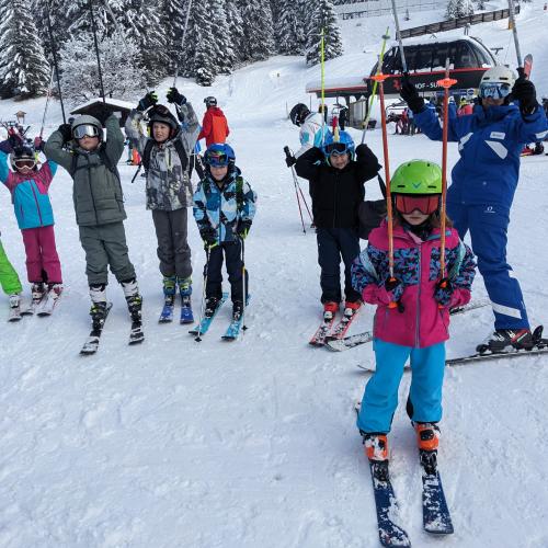 Kindergruppe mit Schilehrerin - Alle halten die Stöcke in die Höhe