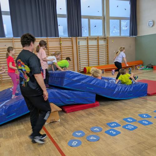Die Kinder laufen, klettern im Turnssal über einen "Dinorücken" gebaut aus den blauen Weichböden