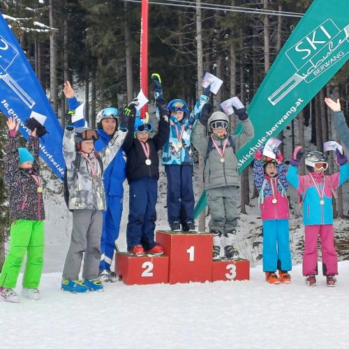 Eine Gruppe Kinder steht auf und um das Siegerpodest nah dem Rennen, mit Schilehrerin und Begleitlehrerin