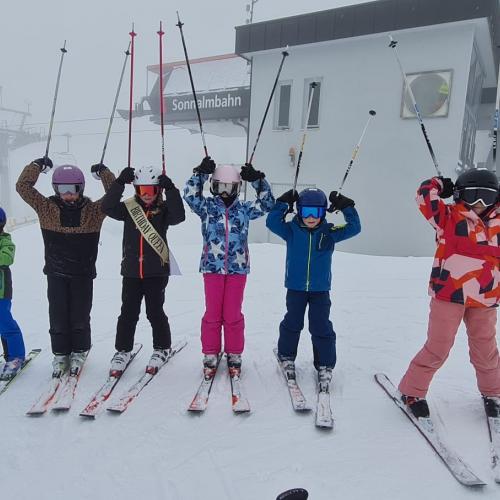  Kinder stehen im Schneetreiben mit erhobenen Stöcken in einer Reihe
