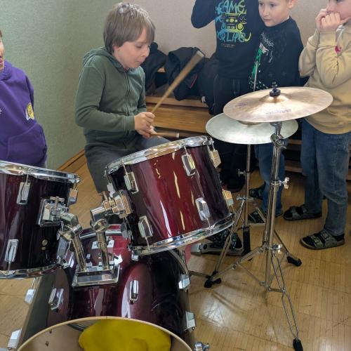 Ein Junge sitzt beim Schlagzeug und spielt  etwas vor (er kann es schon)