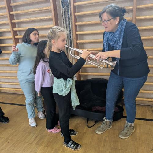 Ein Mädchen versucht das Tenorhorn zu spielen und wir d dabei von eiem Mitglied er MK angeleitet ein weiteres Mädchenwartet