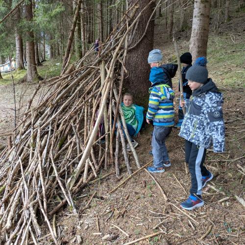 Drei Kinder bei einem Baum, an den mit Stöcken eine Hütte drangebaut ist