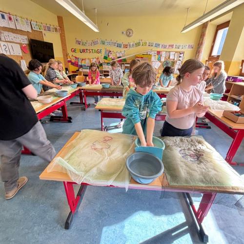 Man sieht den ganzen Klassenraum, an jedem Tisch stehen Kinder und filzen mit Wolle