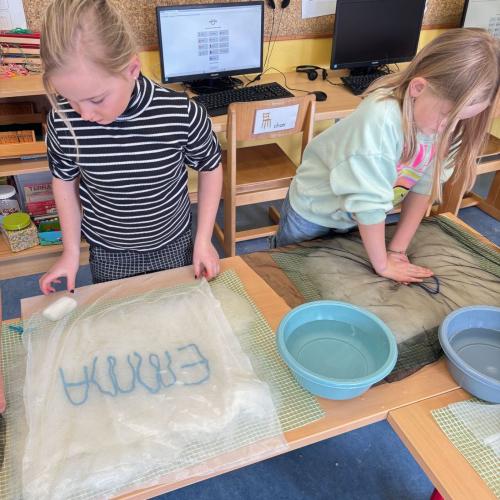Man sieht zwei Kinder, die beim Nassfilzen ihren NAmen auf einen Polster filzen