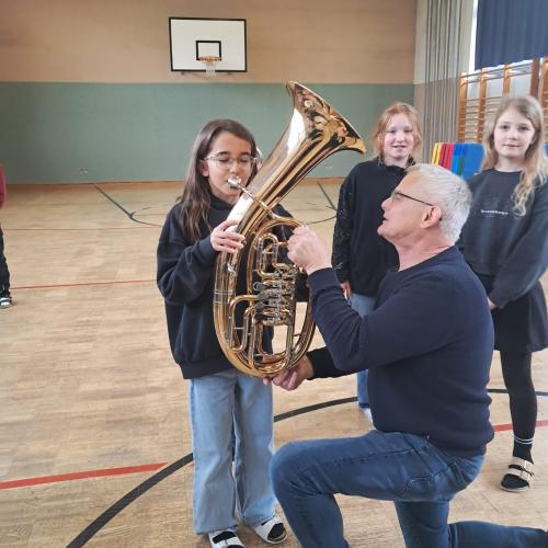 Ein Mädchen versucht dem Kinderbass zu spielen ein Mitglied der MK hilft ihr, zwei weitere Mädchen warten