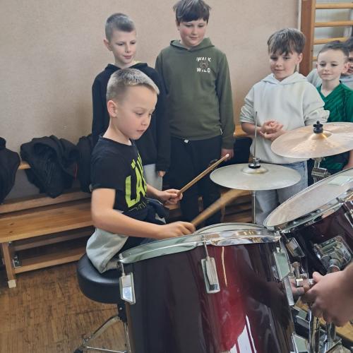 Ein Junge sitzt beim Schlagzeug und probiert, vier weitere Jungen warten 