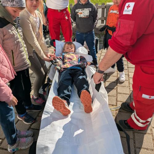 Ein Junge liegt auf der Bahre des Rettungswagens, die am Boden steht, rundherum stehen die MitschülerInnen und die Rettungsmitarbeiter