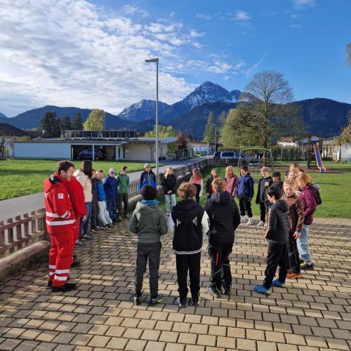 Die Schüler der 4. Klasse stehen im Kreis mit einem Rot KReuz Mitarbeiter im Schulhof