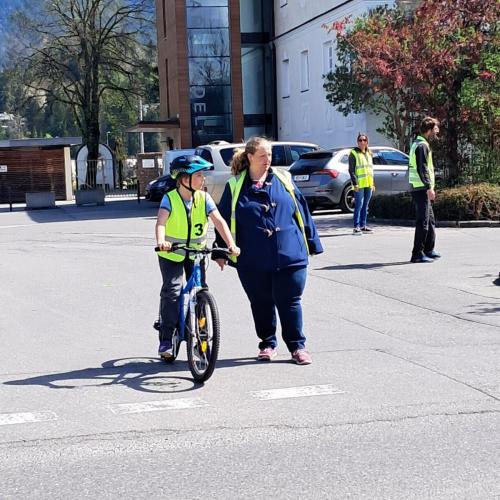 Ein Kind steht mit seinem Fahrrad vor der Haltelinie, beim Widum BReitenwang, nebenihm steht eine Mutter, die als Helferin bei der Radfahrübung dabei ist.